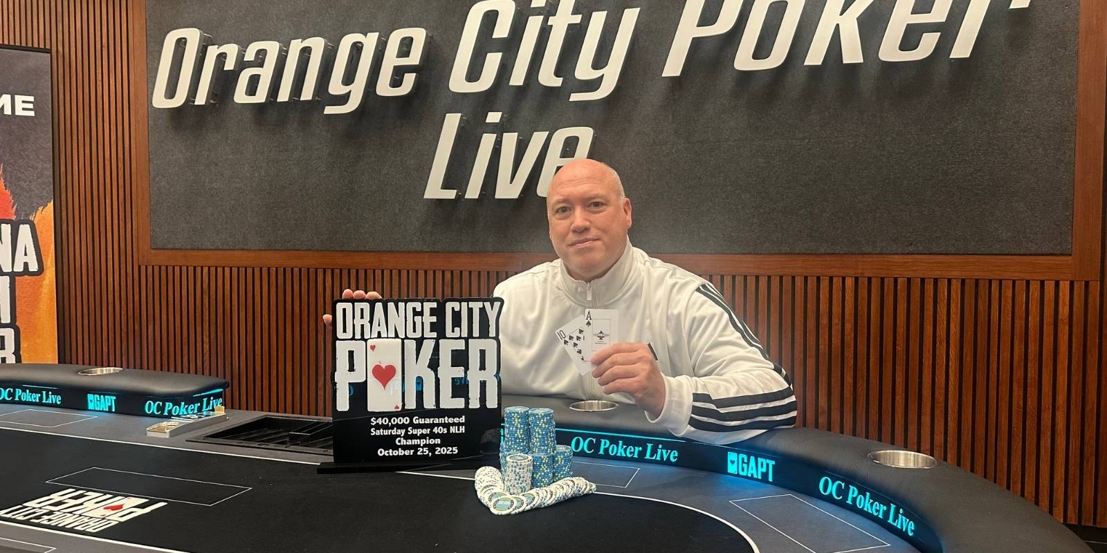 A person sitting at a poker table in front of an orange city poker live sign