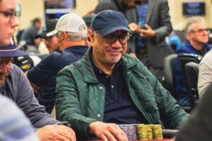 A man in a green jacket and blue hat plays poker.