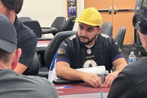 Ezequiel Carranza in yellow hat and Baltimore Ravens jersey, sits at a poker table.