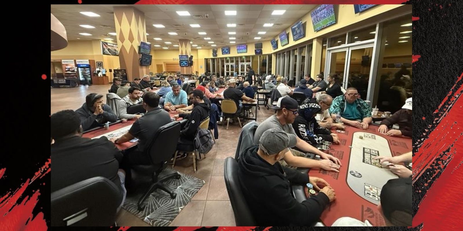 A poker room with many tables and people playing poker under bright lights and several television screens.